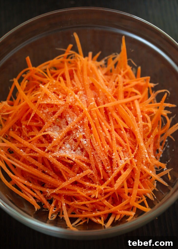 Julienned carrots with salt in a mixing bowl.