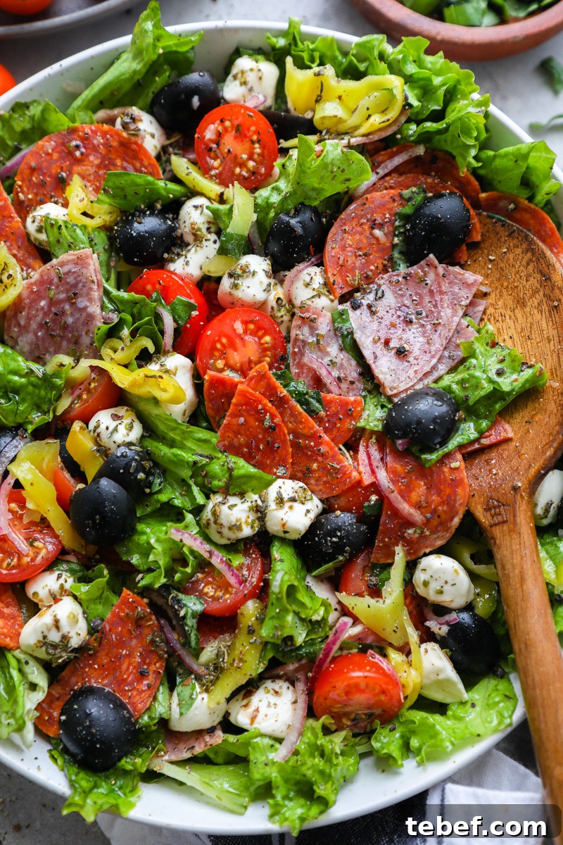 A large white bowl filled with a loaded Italian salad tossed in a homemade red wine vinaigrette