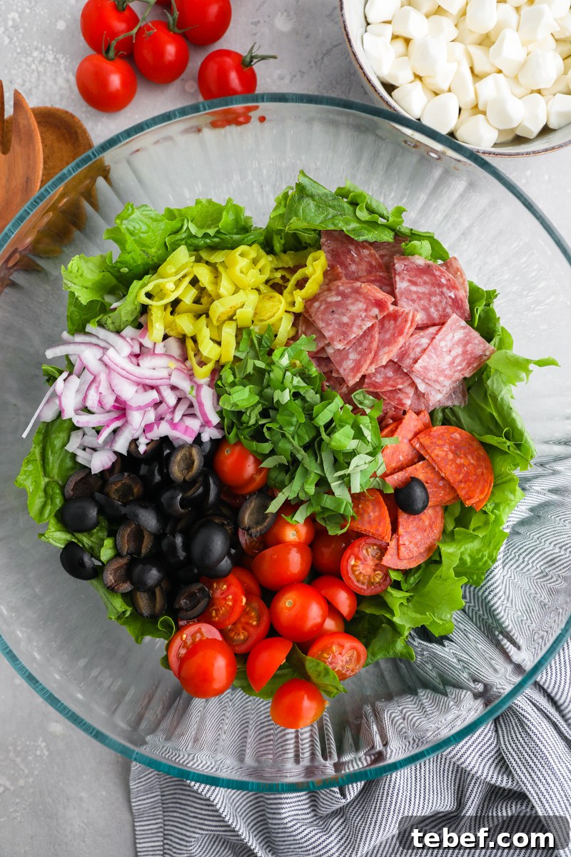 Ingredients for an Italian salad sectioned out in a large clear bowl sitting next to a smaller bowl of fresh mozzarella