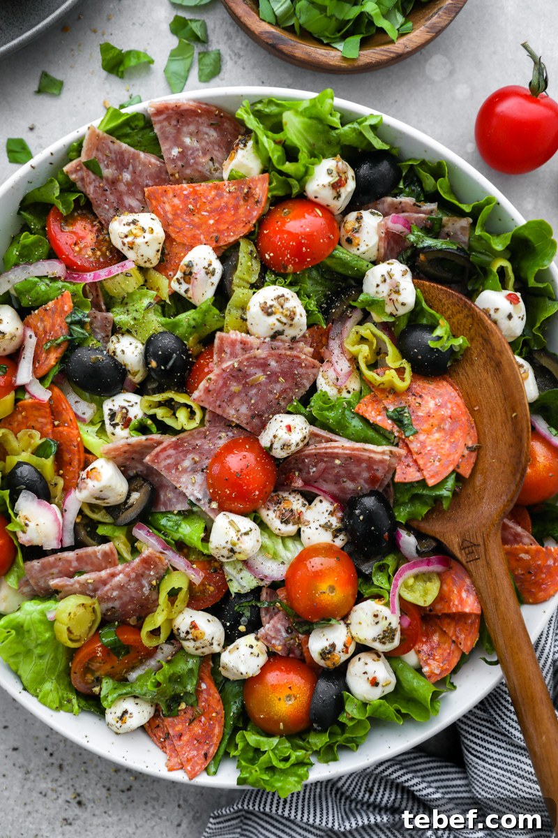 A close up photo of an Italian salad tossed in a homemade red wine vinaigrette with a wooden spoon digging into it