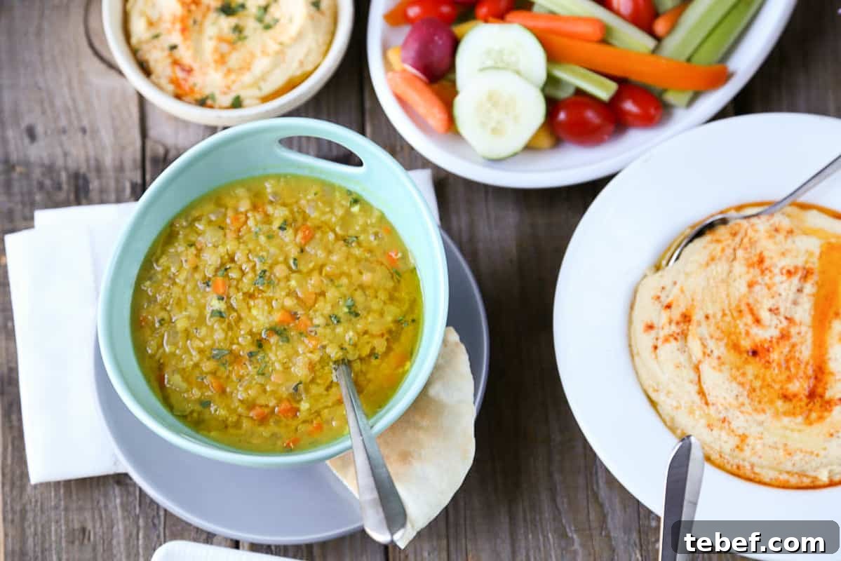 lemon lentil soup in a turquoise bowl on a wooden table with hummus and veggies